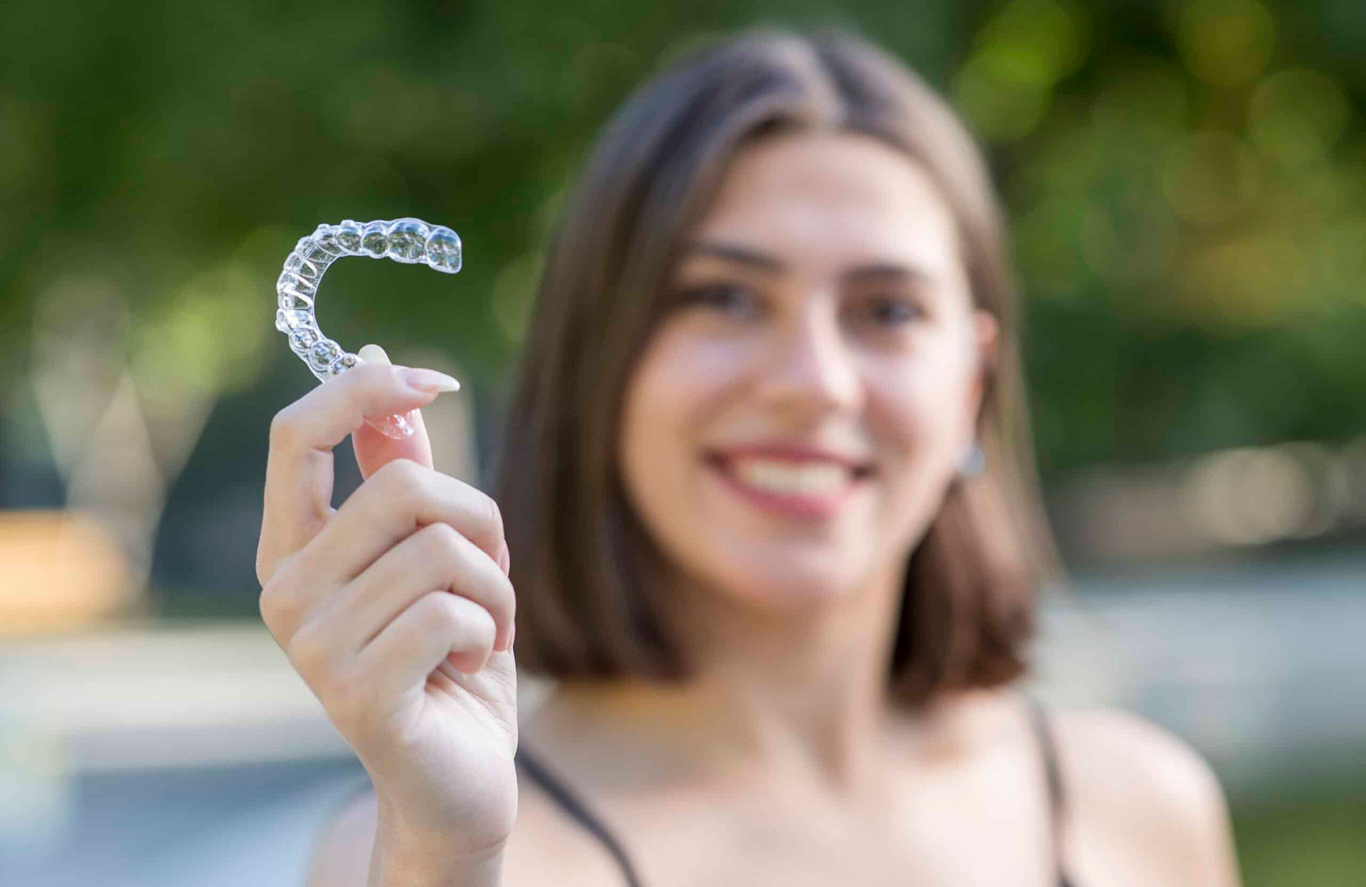 A woman holding up a clear plastic orthodontic appliance with her left hand.