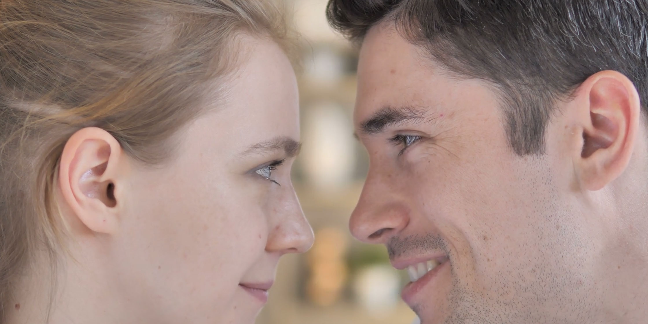 The image features a man and a woman sharing an intimate moment with a close gaze, set against a blurred background.