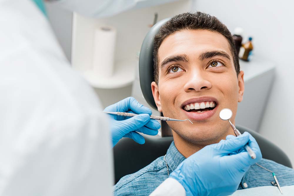 A man sitting in a dental chair with a dentist performing a procedure on him, wearing gloves and using dental tools.