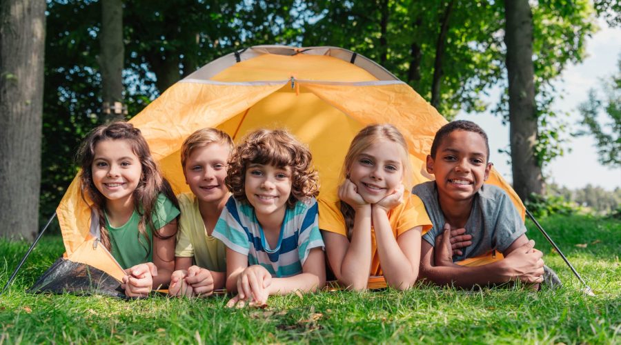 cheerful multicultural kids smiling while lying near camp